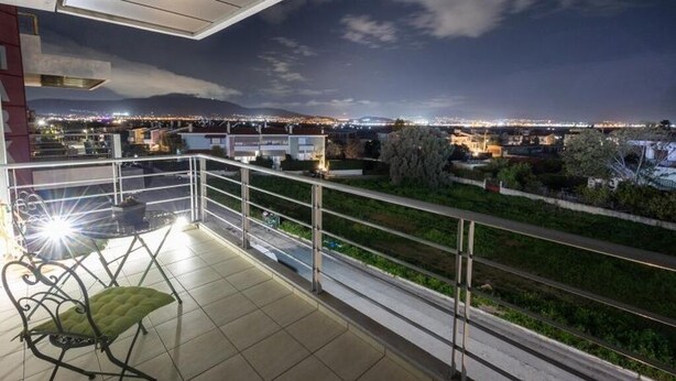 A balcony with a view of a cityscape at night, a chair, and a railing. - A space of comfort and relaxation with a wonderful view and warm hospitality. (Markopoulo Mesogeas)