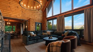 L’intérieur d’une cabane en rondins, avec un grand canapé, un coin repas et une vue sur l’extérieur.