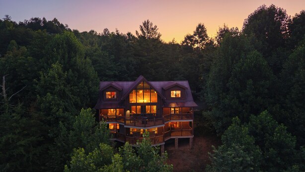 Une cabane en rondins à plusieurs étages, dotée d’un balcon et entourée d’une forêt dense.