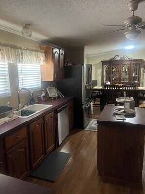 A kitchen with wooden cabinets, a stainless steel refrigerator, a dishwasher, and a dining area with a wooden table and chairs.