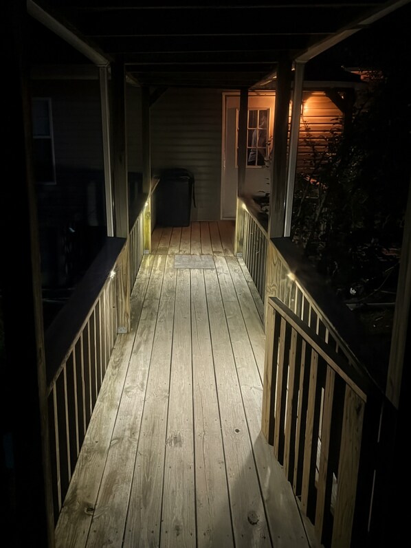 Une terrasse en bois, dotée de rampes, qui mène à une porte et à une fenêtre.