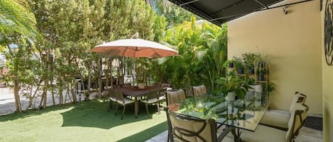 An outdoor patio area with a glass table, chairs, and a large umbrella.
