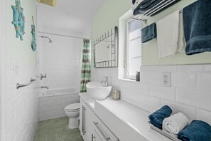 Un bany amb una banyera blanca, un lavabo blanc, un vàter i un mirall amb una barra de tovalloles a sobre.