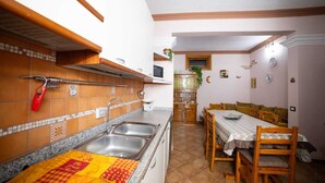 Une cuisine équipée d’un évier, d’une cuisinière et de meubles de rangement en bois. On y trouve une table à manger avec des chaises et une fenêtre.