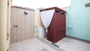 Un petit espace extérieur clos, délimité par un mur de pierre, une porte en métal, un mur ondulé rouge et un étendoir métallique.