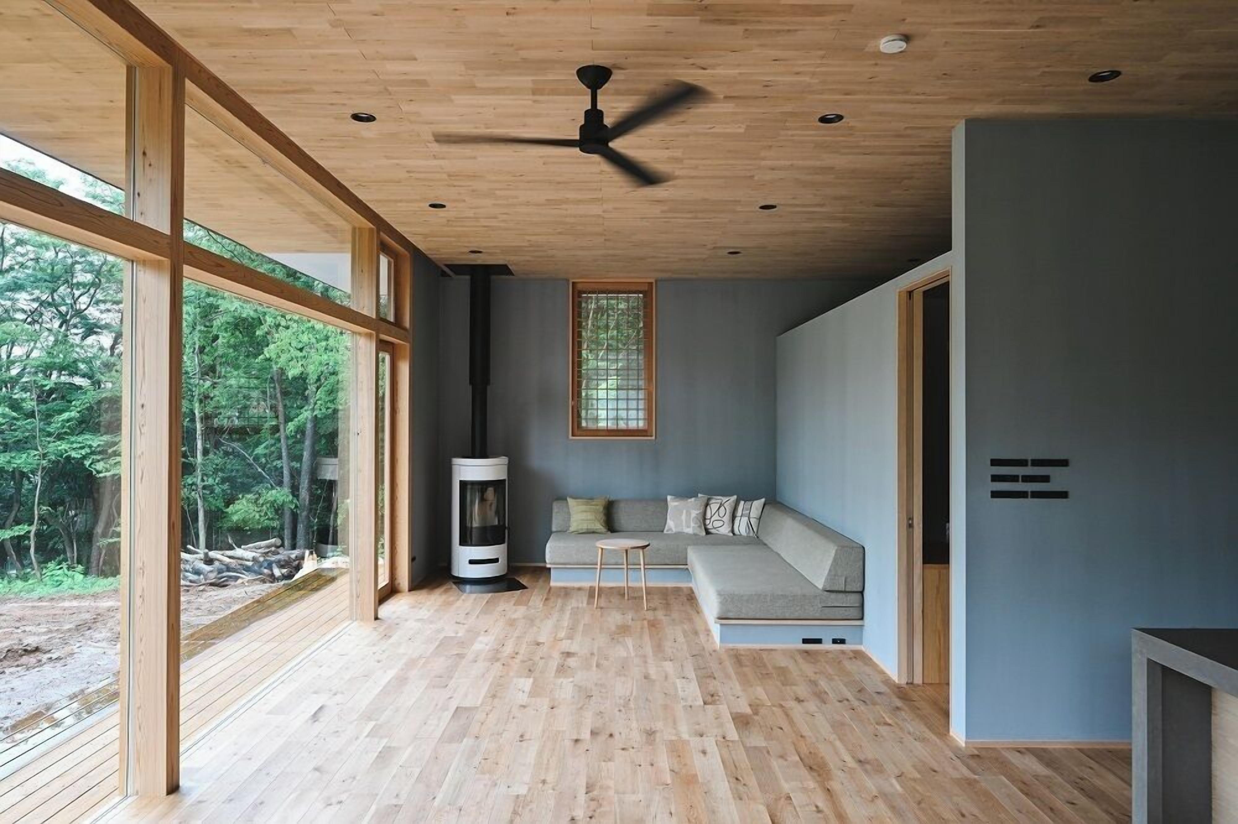 A modern interior with a wooden ceiling, large windows, a built-in fireplace, and a gray sofa.