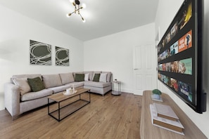 A modern living room with a sectional sofa, a coffee table, and a wall-mounted TV displaying movie posters. - Spacious I Long stays I Sleeps 8 I Free parking (Greater London)