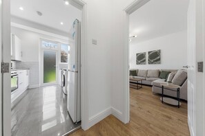 A modern kitchen with a refrigerator, washing machine, and oven, leading to a living area with a sofa and a coffee table. - Spacious I Long stays I Sleeps 8 I Free parking (Greater London)