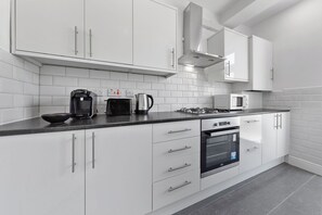 Une cuisine moderne avec des meubles blancs, un plan de travail noir, un four Bosch, une machine à café et un four à micro-ondes.