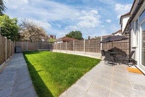 A backyard with a paved patio, a lawn, and a wooden fence. - Spacious I Long stays I Sleeps 8 I Free parking (Greater London)