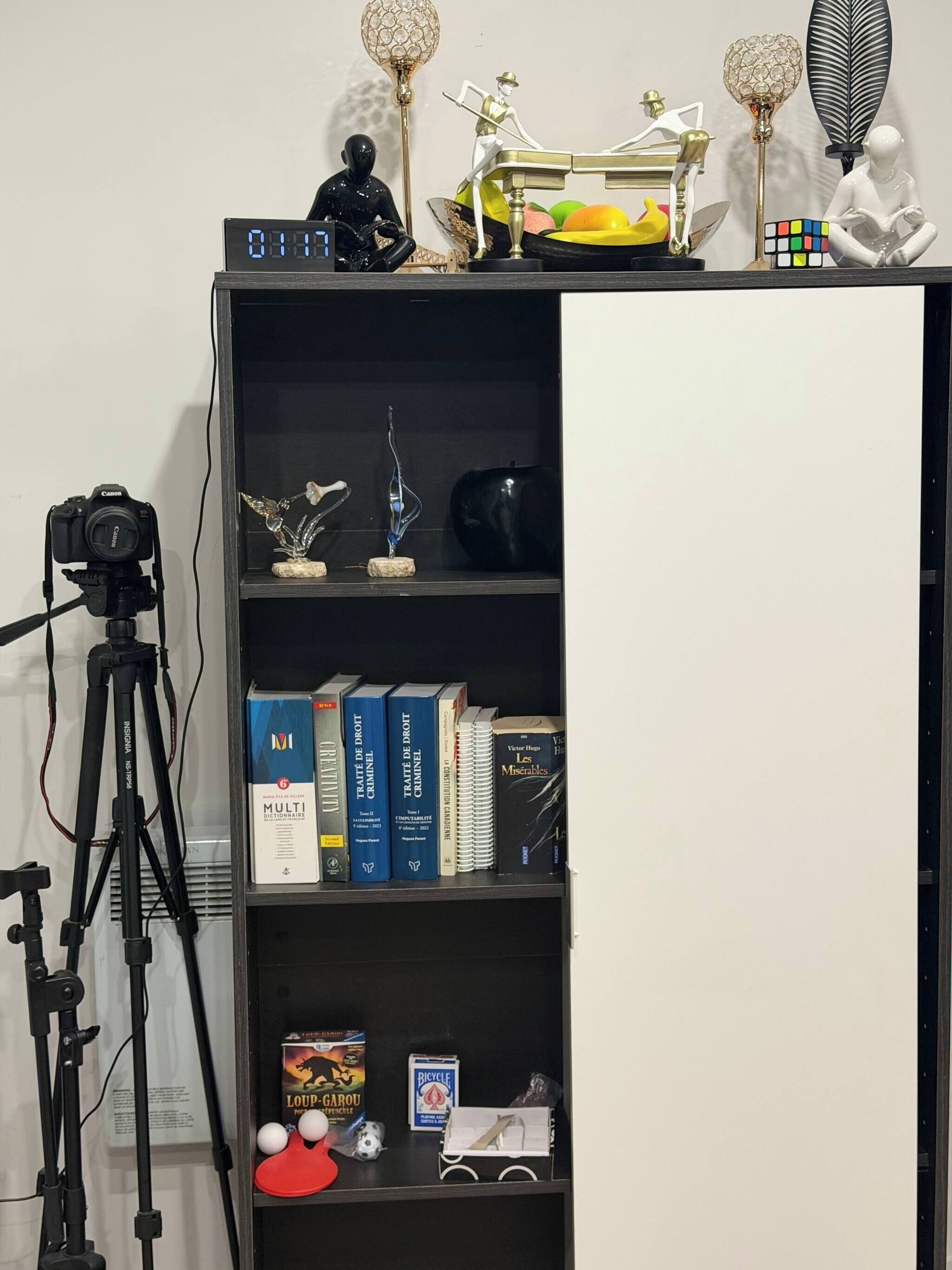 Uma estante com diversos objetos, incluindo livros, uma câmera sobre um tripé e itens decorativos.