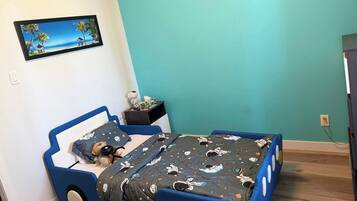 Une chambre d’enfant avec un lit, une table de chevet, un tableau accroché au mur et un plancher en bois.