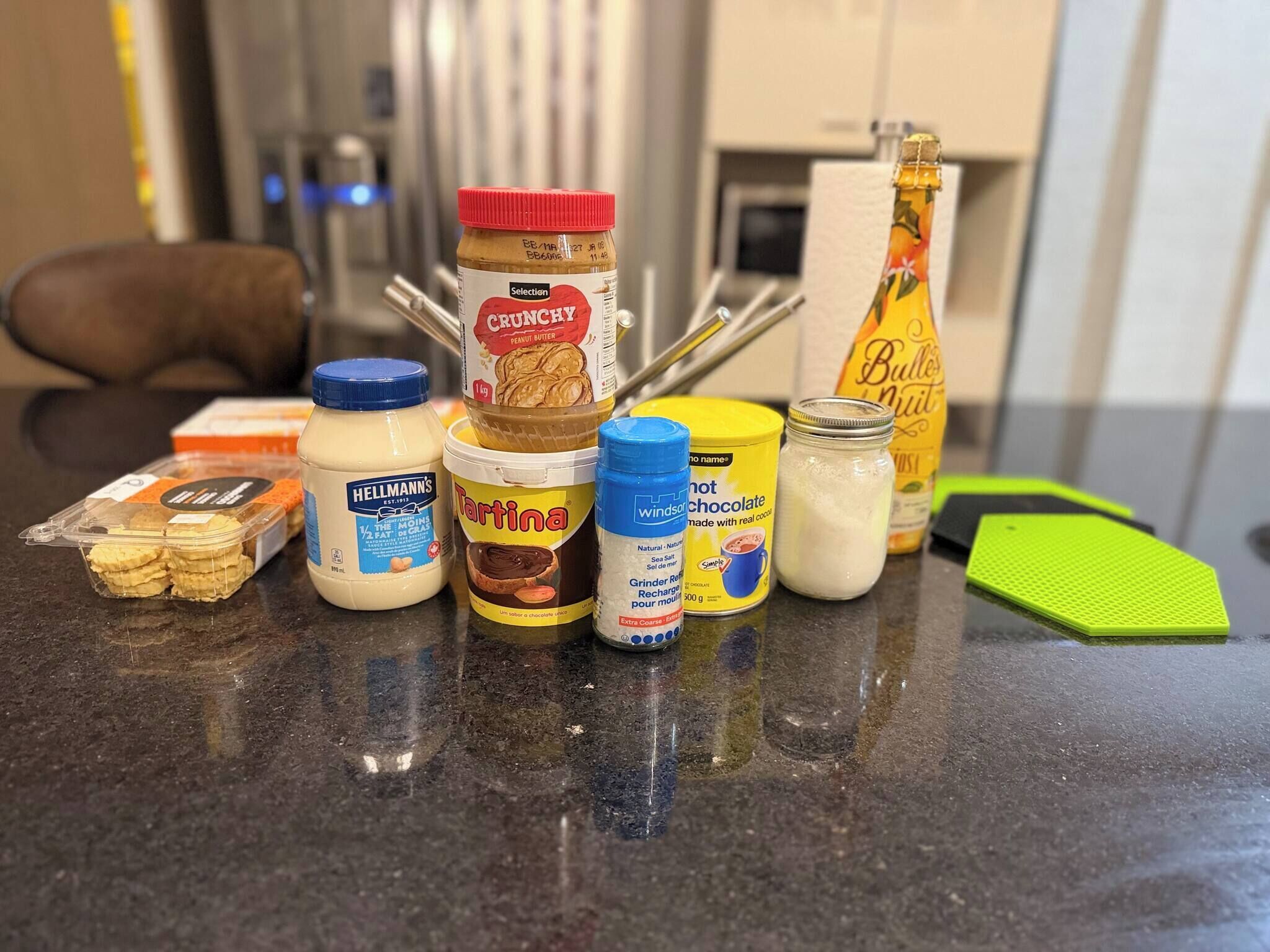 A kitchen counter with various food items including jars of peanut butter, chocolate, and a bottle of wine.