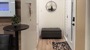 A hallway with a wooden floor, a small table with a plant, a bench, a wall-mounted light fixture, and a door with a frosted glass panel. - Chris Manor (Saint-Augustin-de-Desmaures)