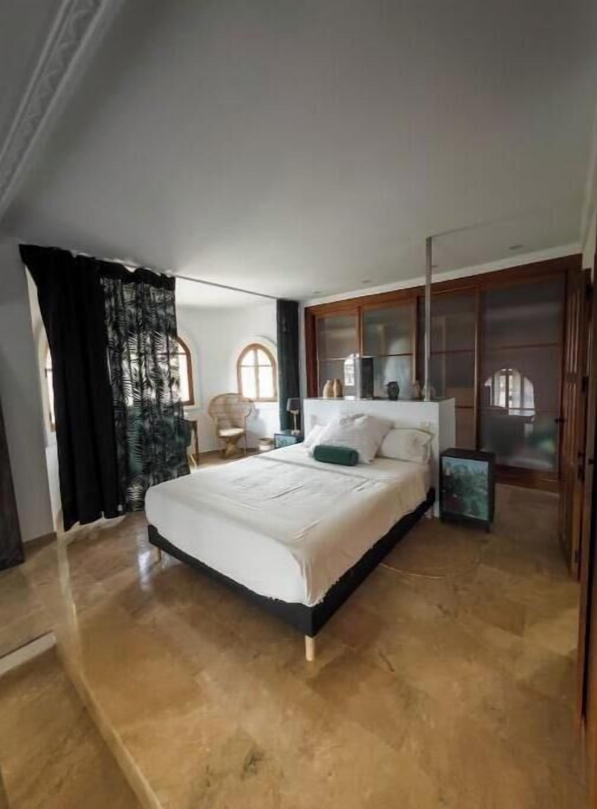 A bedroom with a large bed, a wooden wardrobe, and a small bedside table.