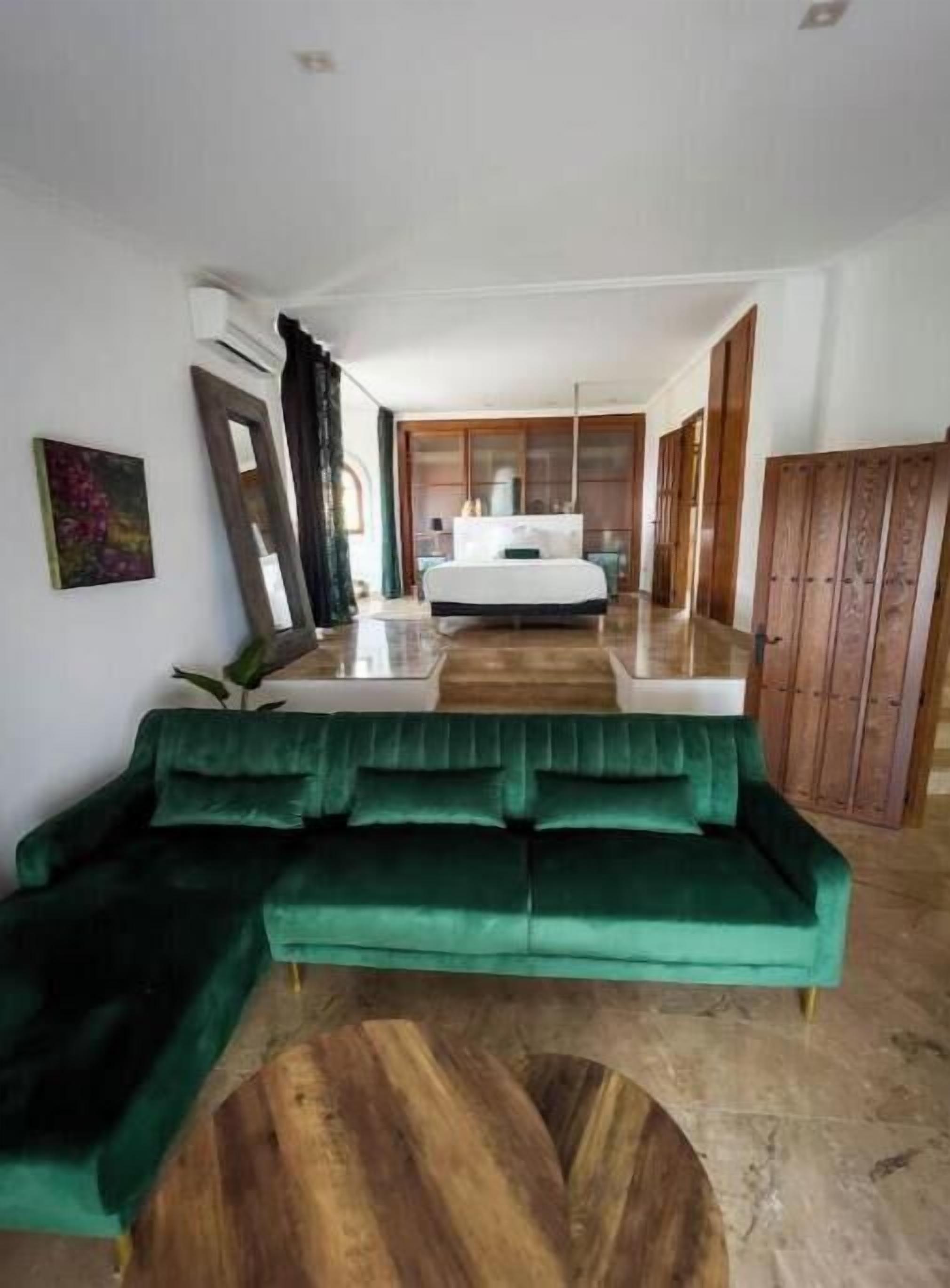 Une chambre d’hôtel avec un canapé vert, une table basse en bois et un lit doté d’une tête de lit blanche.
