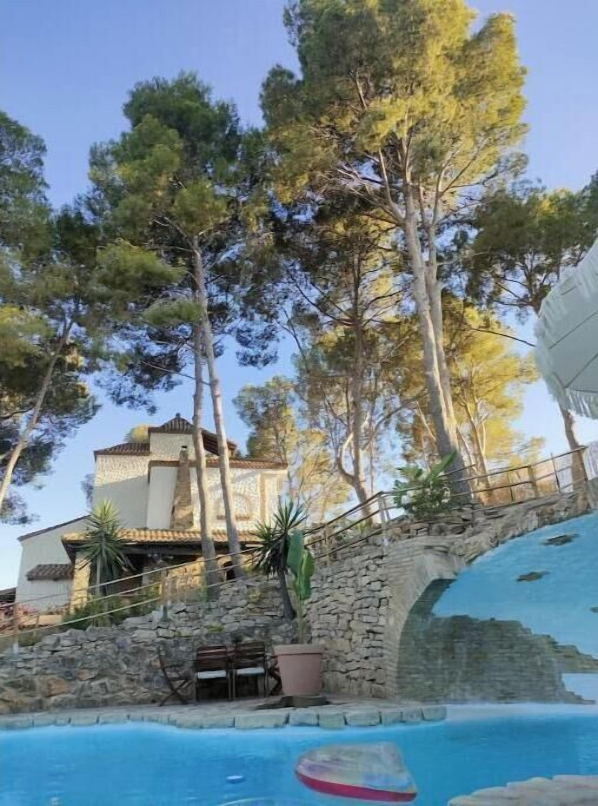 Un espace piscine agrémenté d’un mur en pierre, d’une chaise longue et d’un bâtiment doté d’un toit en tuiles.