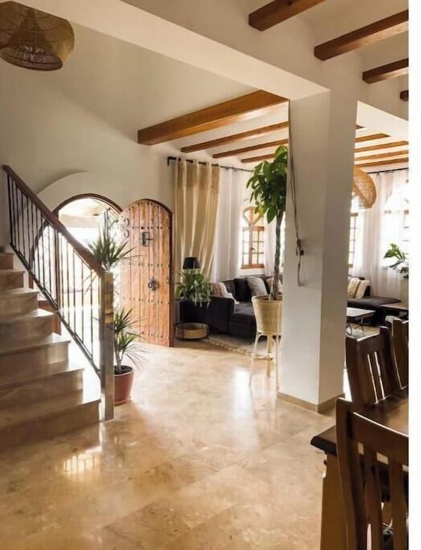A spacious living area with a staircase, wooden beams, a sofa, and a dining table.