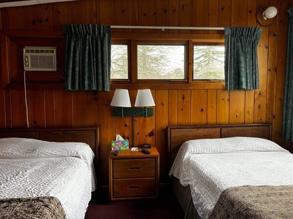 Une chambre avec deux lits, une table de chevet avec une lampe, une fenêtre avec des rideaux et un climatiseur fixé au mur.