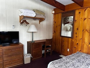 Une pièce comprenant un lit, un bureau avec une chaise, une télévision, une lampe, un miroir et un panneau mural en bois.
