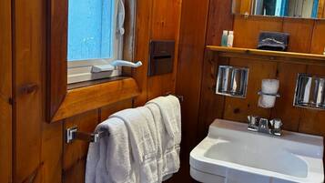 Un baño con paneles de madera, un lavamanos blanco, un perchero, un espejo y una ventana.