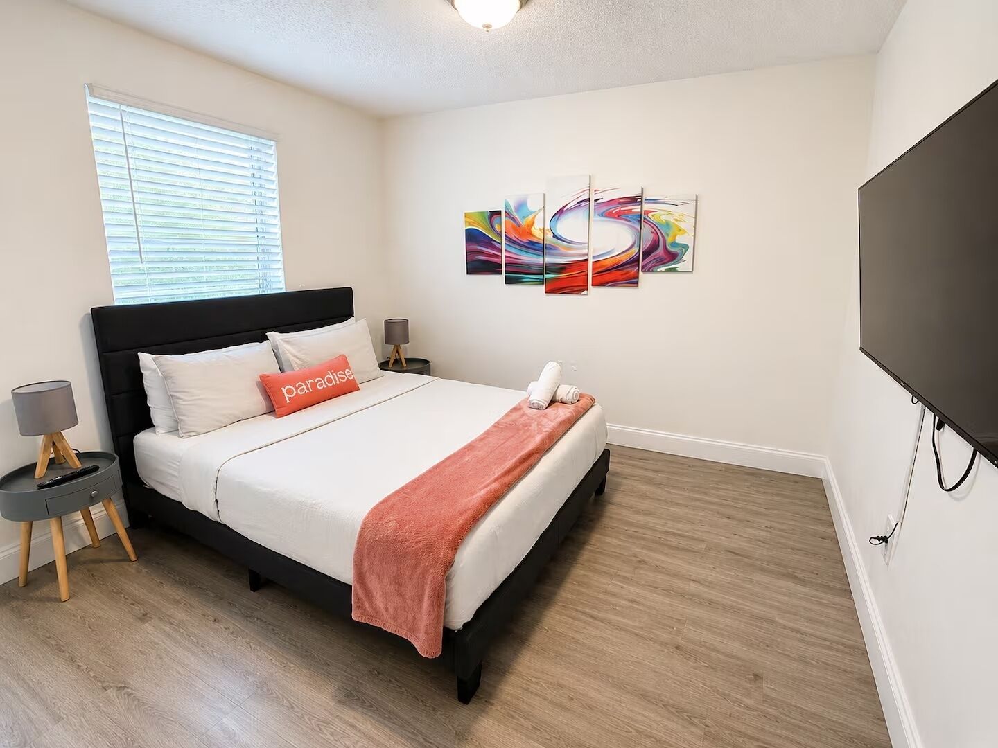 Une chambre à coucher moderne avec un lit, un téléviseur et des œuvres d’art accrochées au mur.