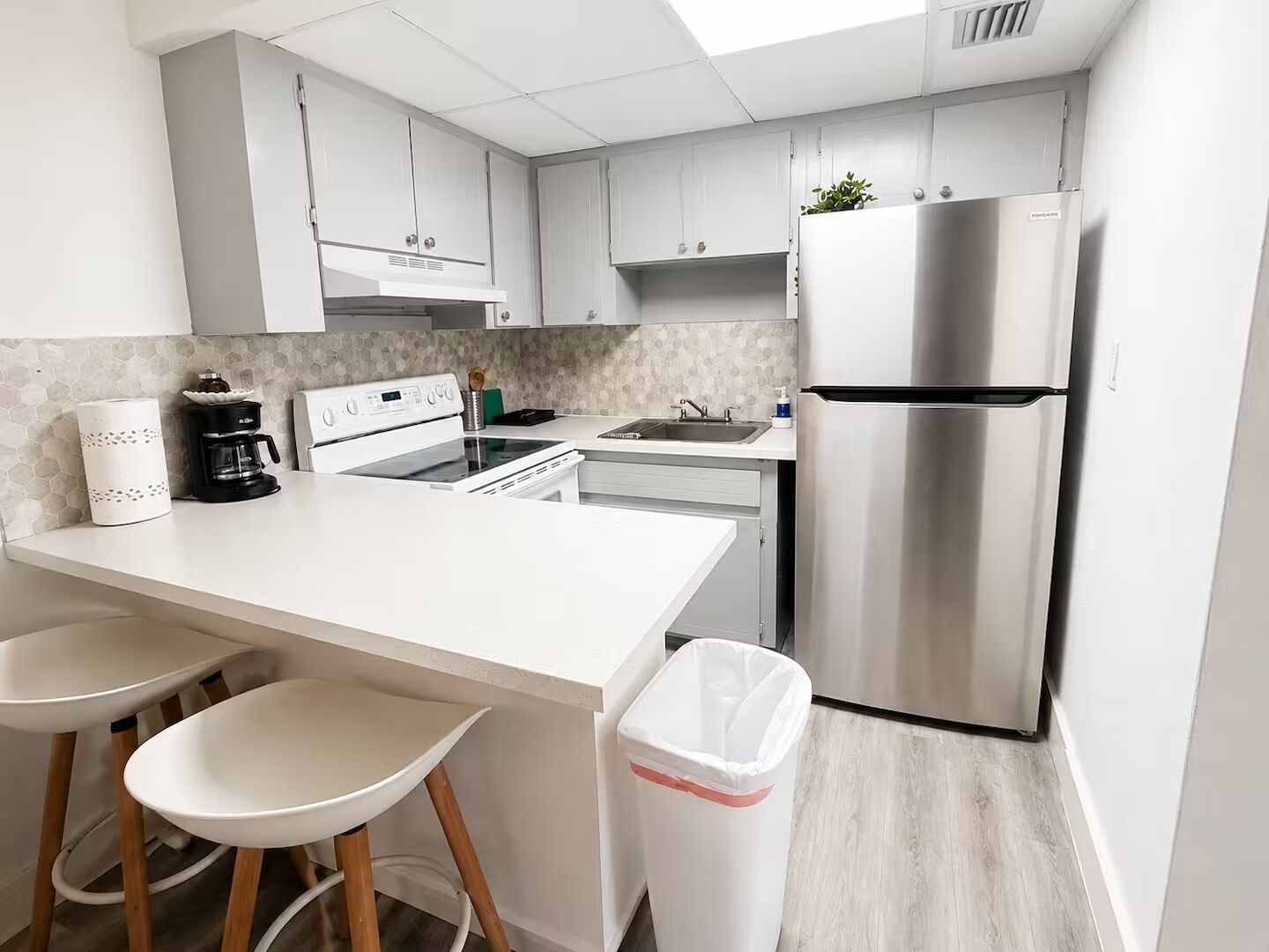 Een moderne keuken met een wit aanrecht, roestvrijstalen apparatuur en een prullenbak.