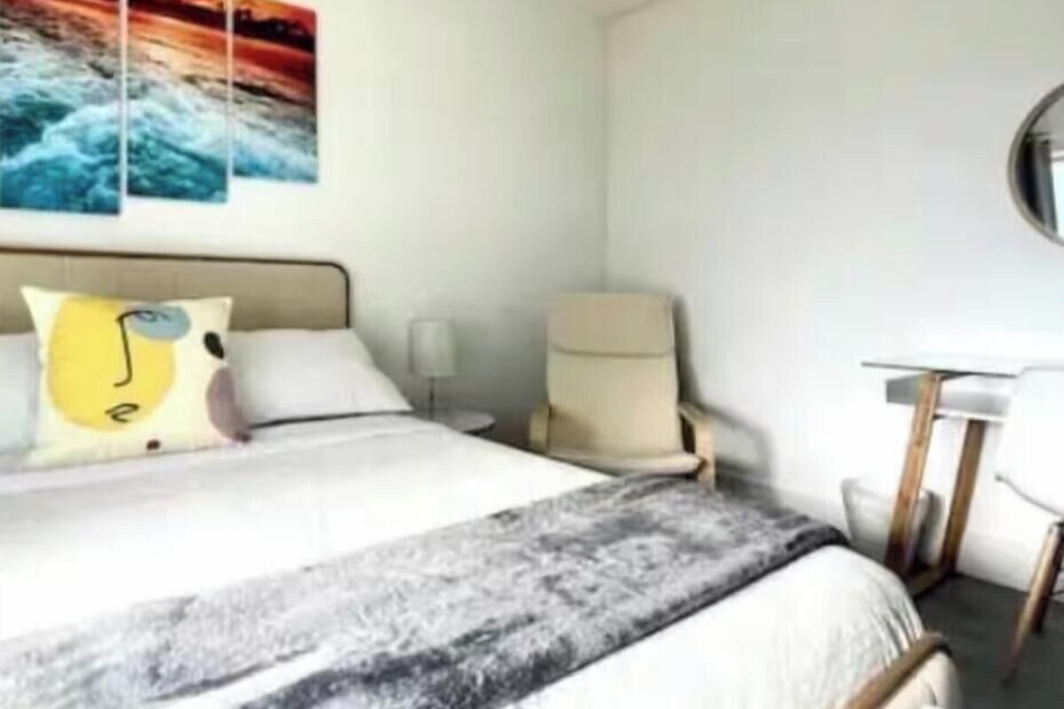 A hotel room with a bed, a chair, a desk, and wall art.