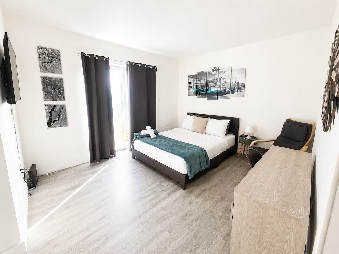 A hotel room with a bed, a desk, a chair, and artwork on the walls.