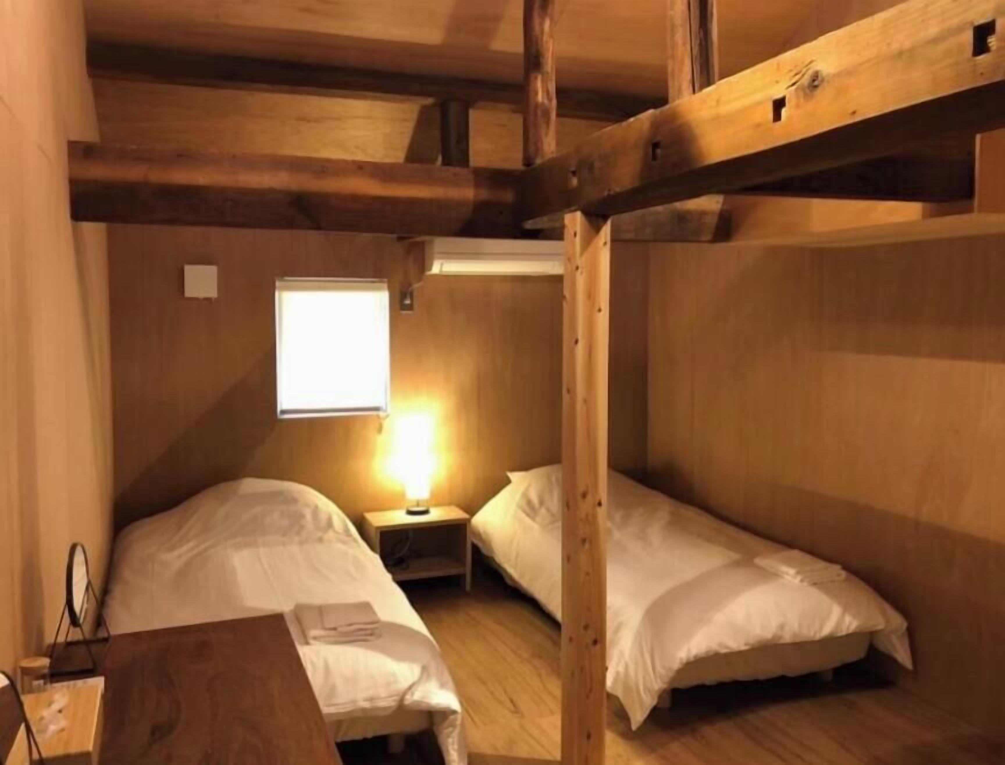 A room with two bunk beds, a bedside table with a lamp, and a window providing natural light.