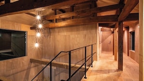 Interior de madera con escalera, barandilla de vidrio y vigas a la vista.