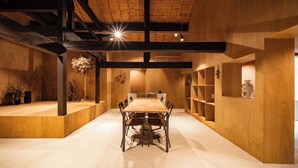 Una habitación amplia con una mesa y sillas de madera, techo alto con vigas a la vista y estanterías empotradas de madera con objetos decorativos.