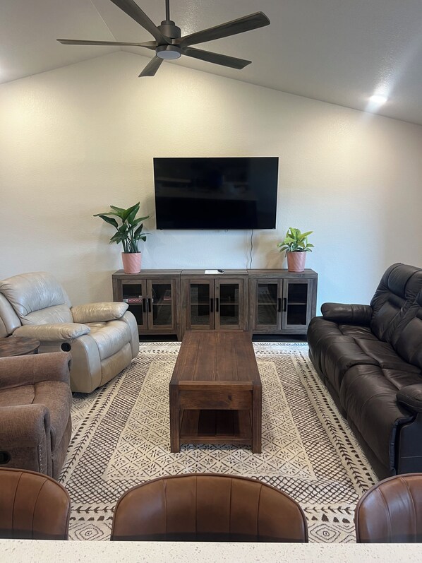 A living room with a flat-screen TV, leather sofas, a wooden coffee table, and a ceiling fan.
