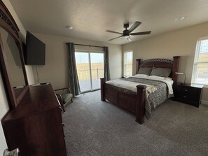 A bedroom with a bed, a ceiling fan, a TV, a dresser, a nightstand, and a window with blinds.