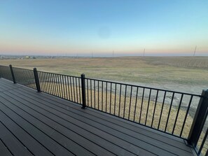 A wooden deck with a metal railing overlooking a flat landscape with distant power lines.