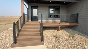 Een modern huis met een houten terras, een zwarte deur en een raam.