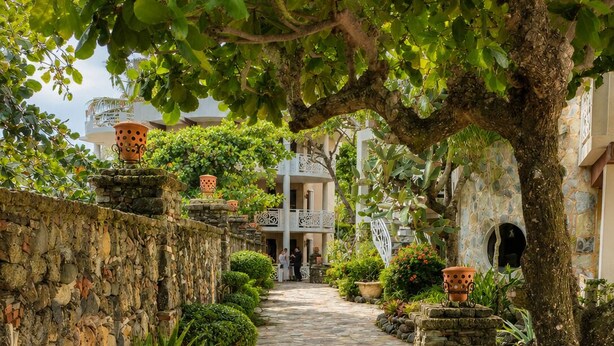 A stone pathway leading to a building with a balcony, surrounded by greenery and potted plants. - Ocean View 1BR Condo, Beach, Pool & Jacuzzi (Cabarete)