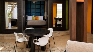 A modern interior with a stone floor, a central round table, white chairs, a sofa with cushions, and a large window. - Ocean View 1BR Condo, Beach, Pool & Jacuzzi (Cabarete)