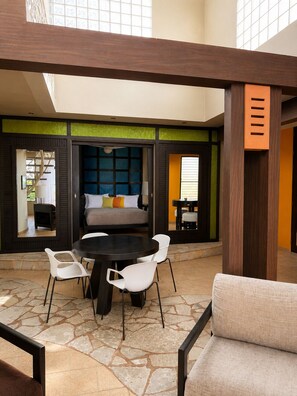 A modern interior with a stone floor, a central round table, white chairs, a sofa with cushions, and a large window. - Ocean View 1BR Condo, Beach, Pool & Jacuzzi (Cabarete)