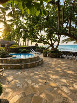 A stone pool surrounded by lounge chairs, a stone wall, and tropical foliage. - Ocean View 1BR Condo, Beach, Pool & Jacuzzi (Cabarete)