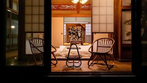 A traditional Japanese room with tatami flooring, a low table, two chairs, and a bed with a floral headboard. - Kominka No Yado Wagoromo (Otaki)