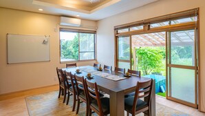 A conference room with a large table, chairs, a whiteboard, and large windows with a view of greenery. - Kominka No Yado Wagoromo (Otaki)