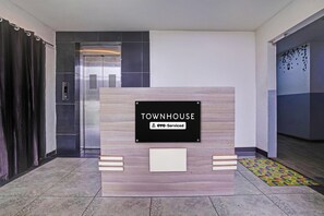 A reception desk with a sign reading 'TOWNHOUSE YO0-Serviced' in a modern lobby with an elevator and patterned flooring. - Deluxe Chandlodiya Railway (Ahmedabad)