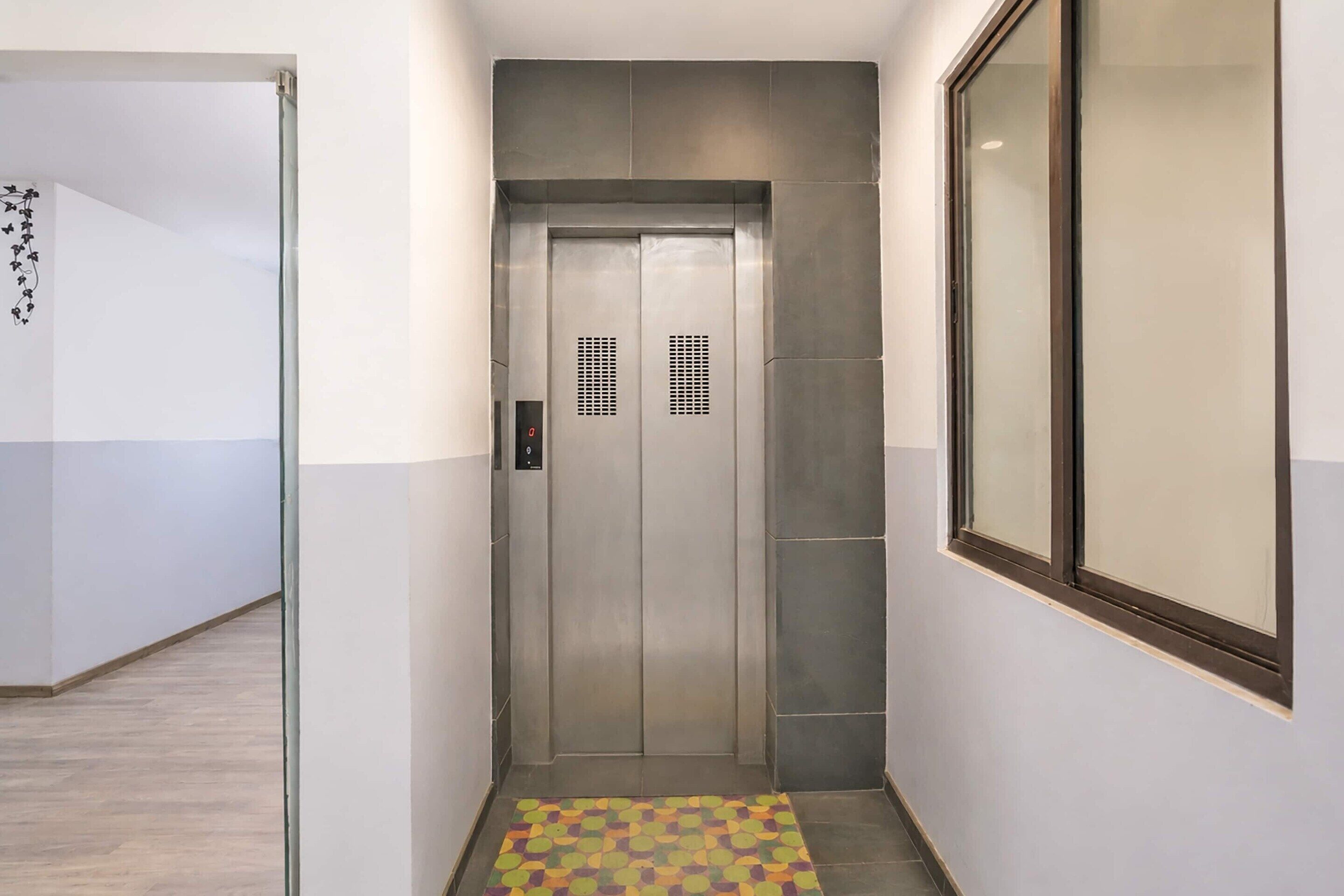 A narrow hallway with a tiled floor, a door with a digital display, and a window on the right.