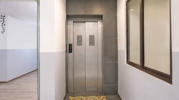 A narrow hallway with a tiled floor, a door with a digital display, and a window on the right.