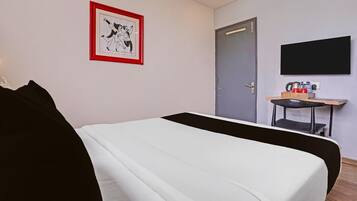 A hotel room with a bed, a desk with a chair, a television, and a door.