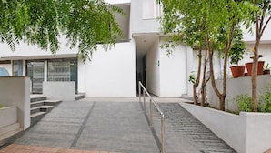 A modern building with a staircase leading to an entrance, surrounded by greenery and potted plants.