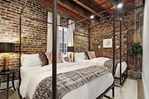 A room with a brick wall, a four-poster bed, a window, and a plant. - Luxe 8BR CBD Duplex, Private Courtyard (New Orleans)