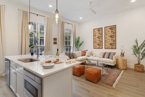 A modern kitchen with a central island, a dining area with a sofa, and two wall-mounted artworks. - Luxe 8BR CBD Duplex, Private Courtyard (New Orleans)