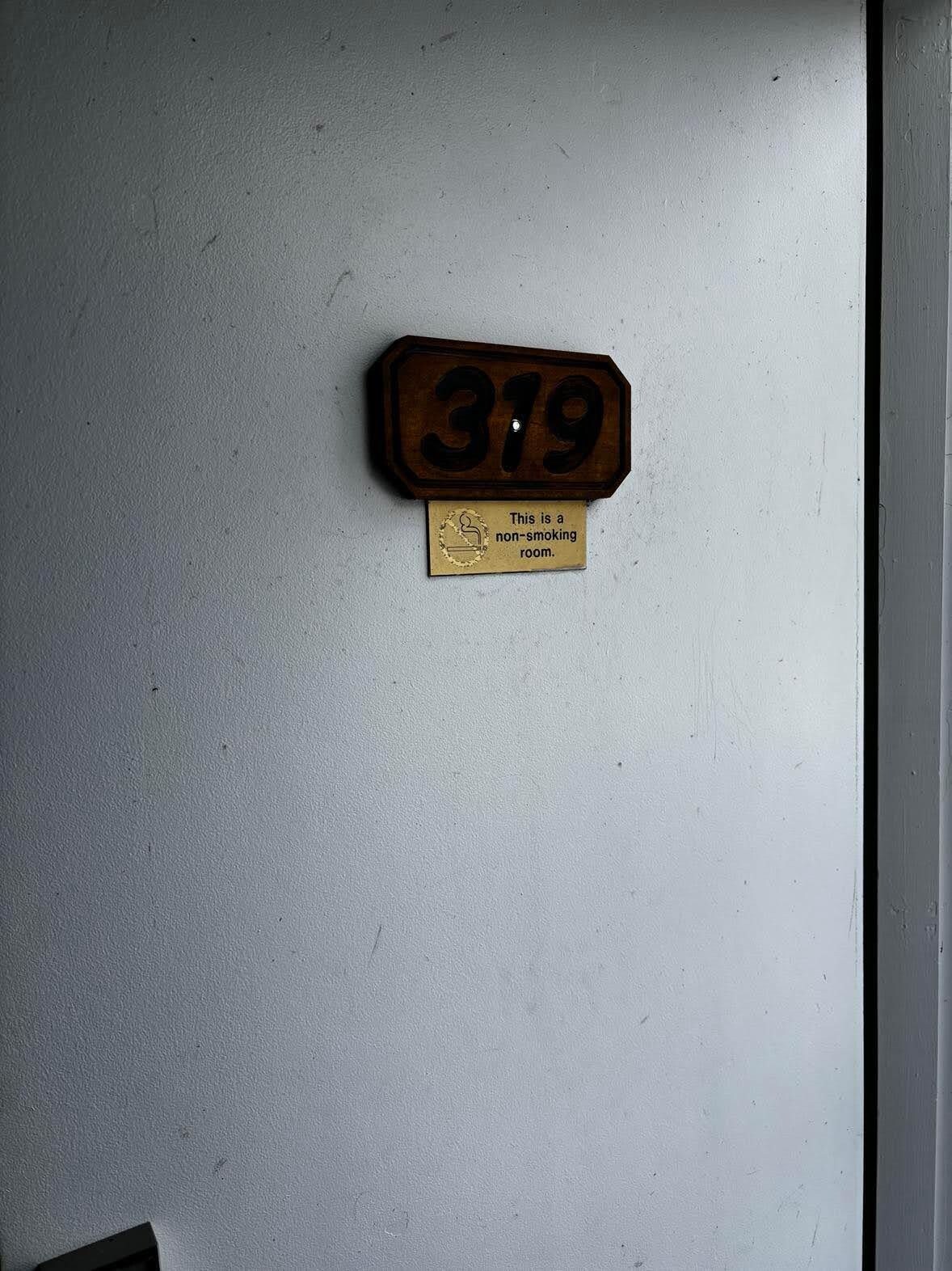 A wooden number plaque with '319' on a white wall, below which is a non-smoking sign.